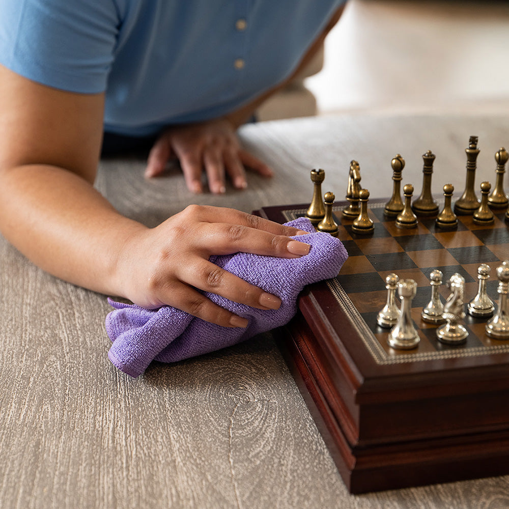 cleaner using a microfiber towel to wipe a wooden chess set