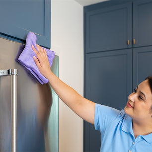 cleaner using a microfiber towel to wipe a stainless fridge