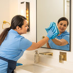 cleaning lady wiping a mirror in a bathroom with a microfiber cloth