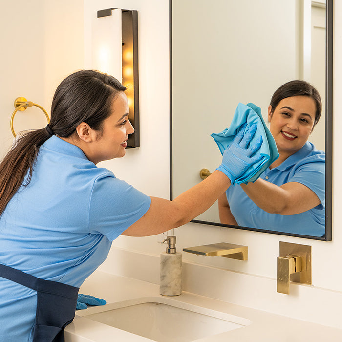 cleaning lady wiping a mirror in a bathroom with a microfiber cloth