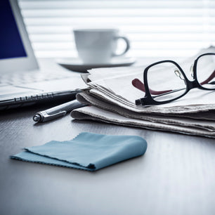 lens cloth, glasses, and newspaper on a desk