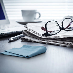 silk lens cloth on a desk with glasses, newspaper and laptop